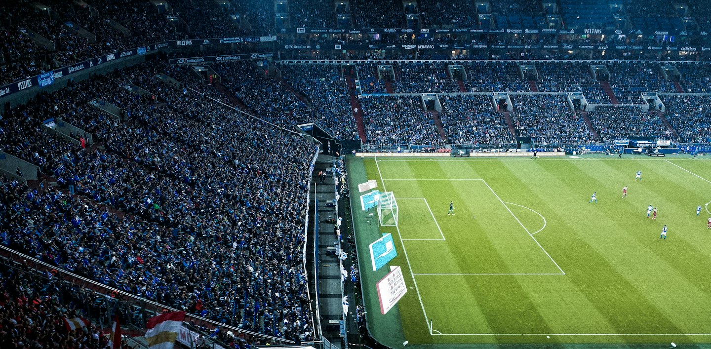 Soccer players compete on a brightly lit field during a night game.