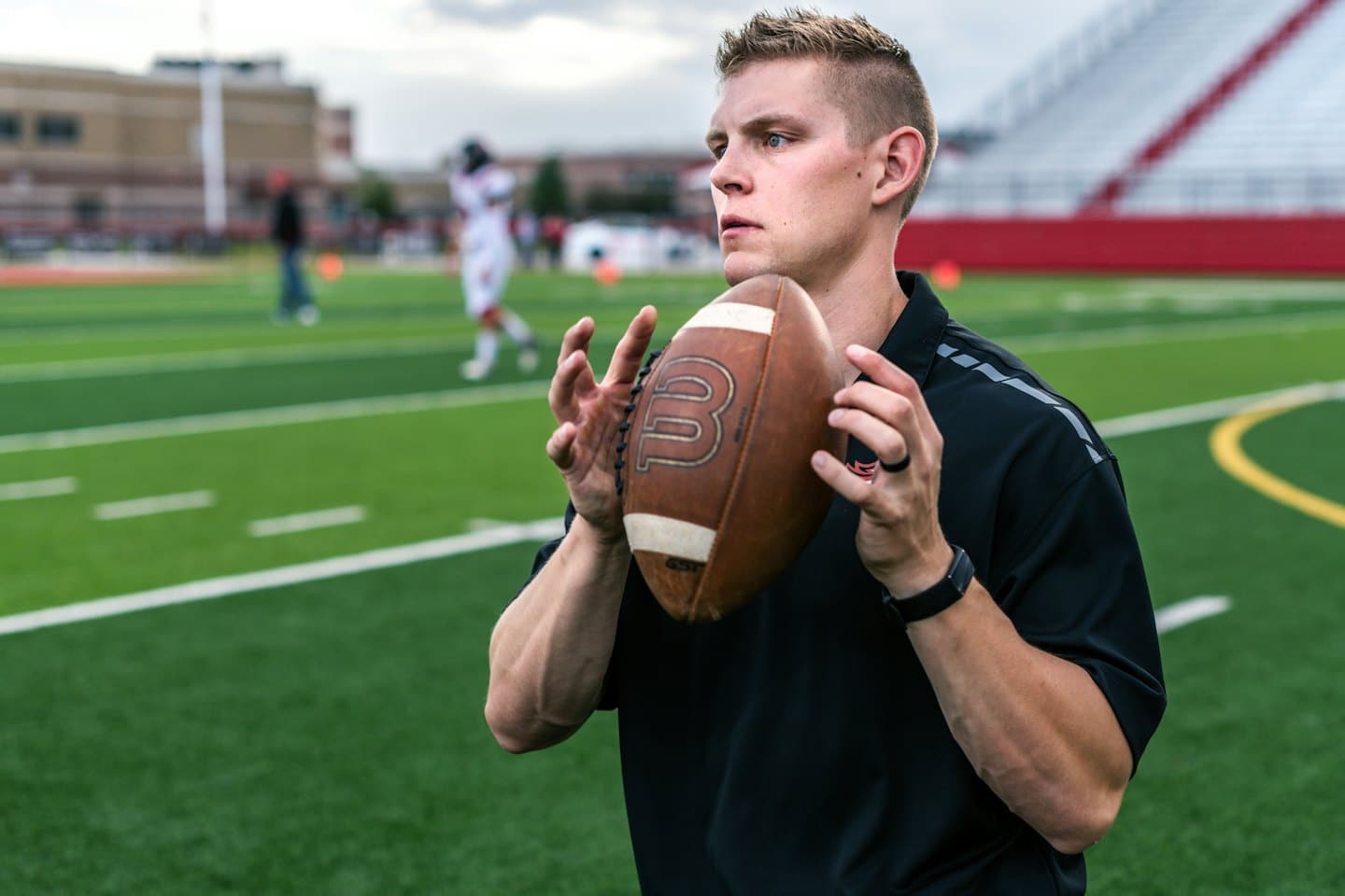Man holding a football on a green turf field.